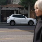 Woman walking in the foreground with a white Mazds CX-5 in the background